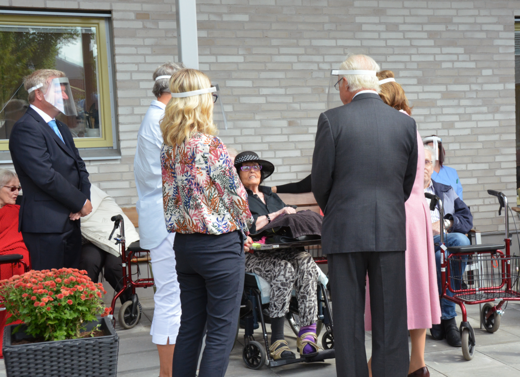 Kungaparet i samtal med äldre kvinna i hatt och rullstol