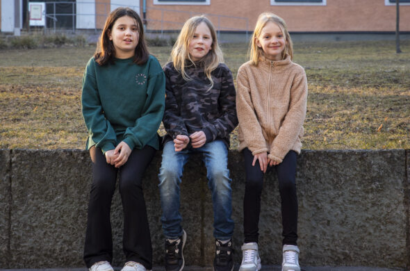 Tre barn sitter på stenmur.