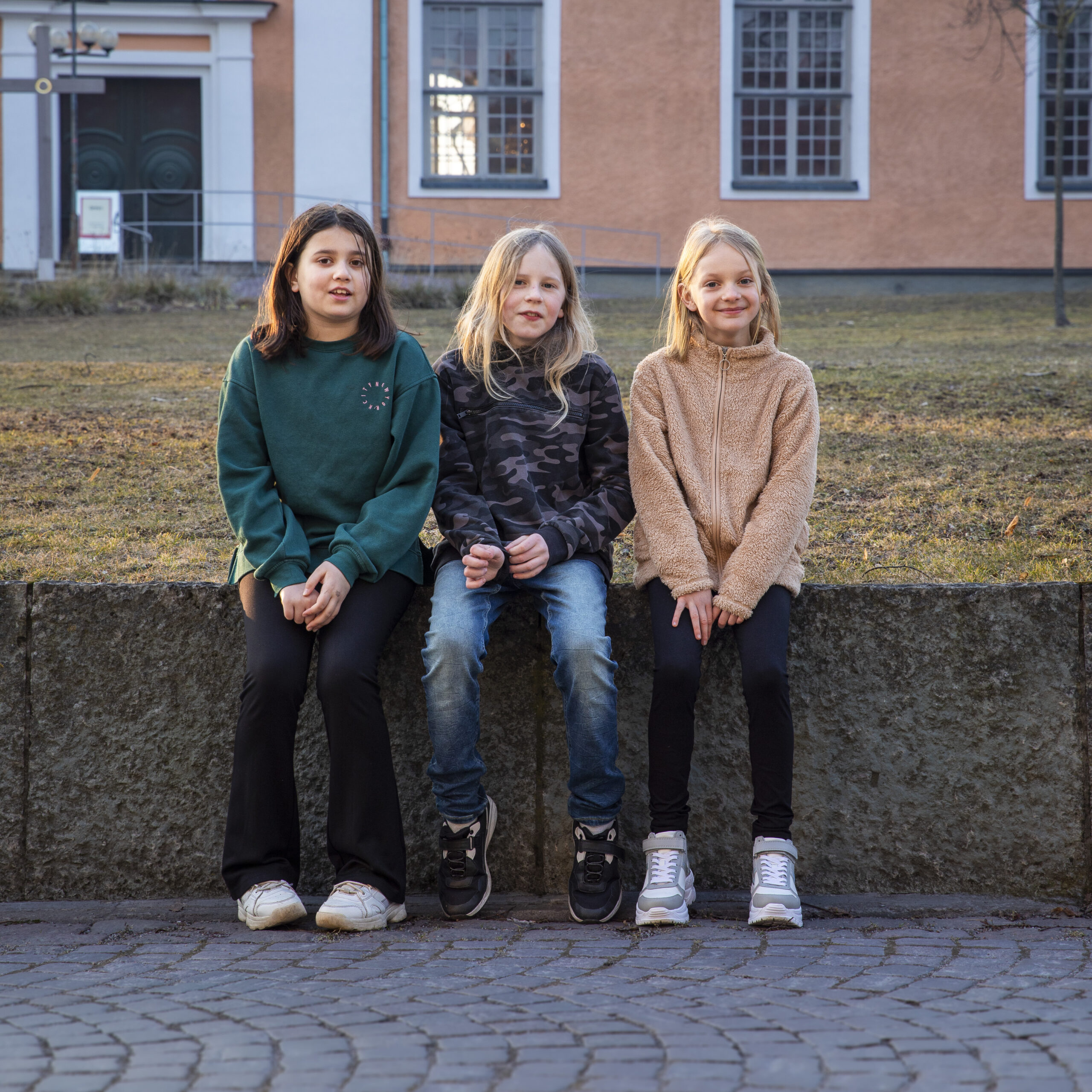 Tre barn sitter på stenmur.