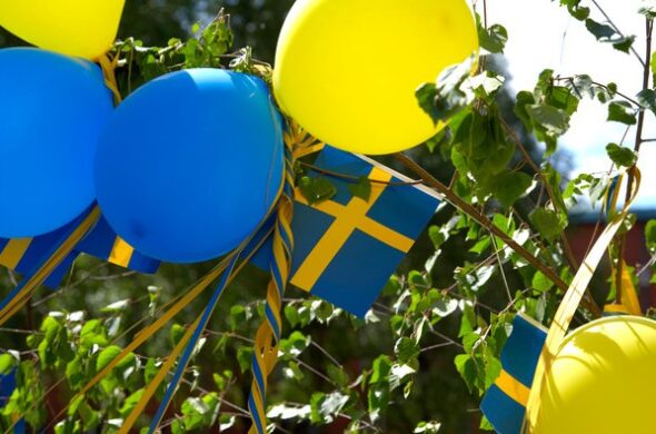 Fem ballonger i gult och blått, och vimpel med svenska flaggan är uppsatt i björkris.