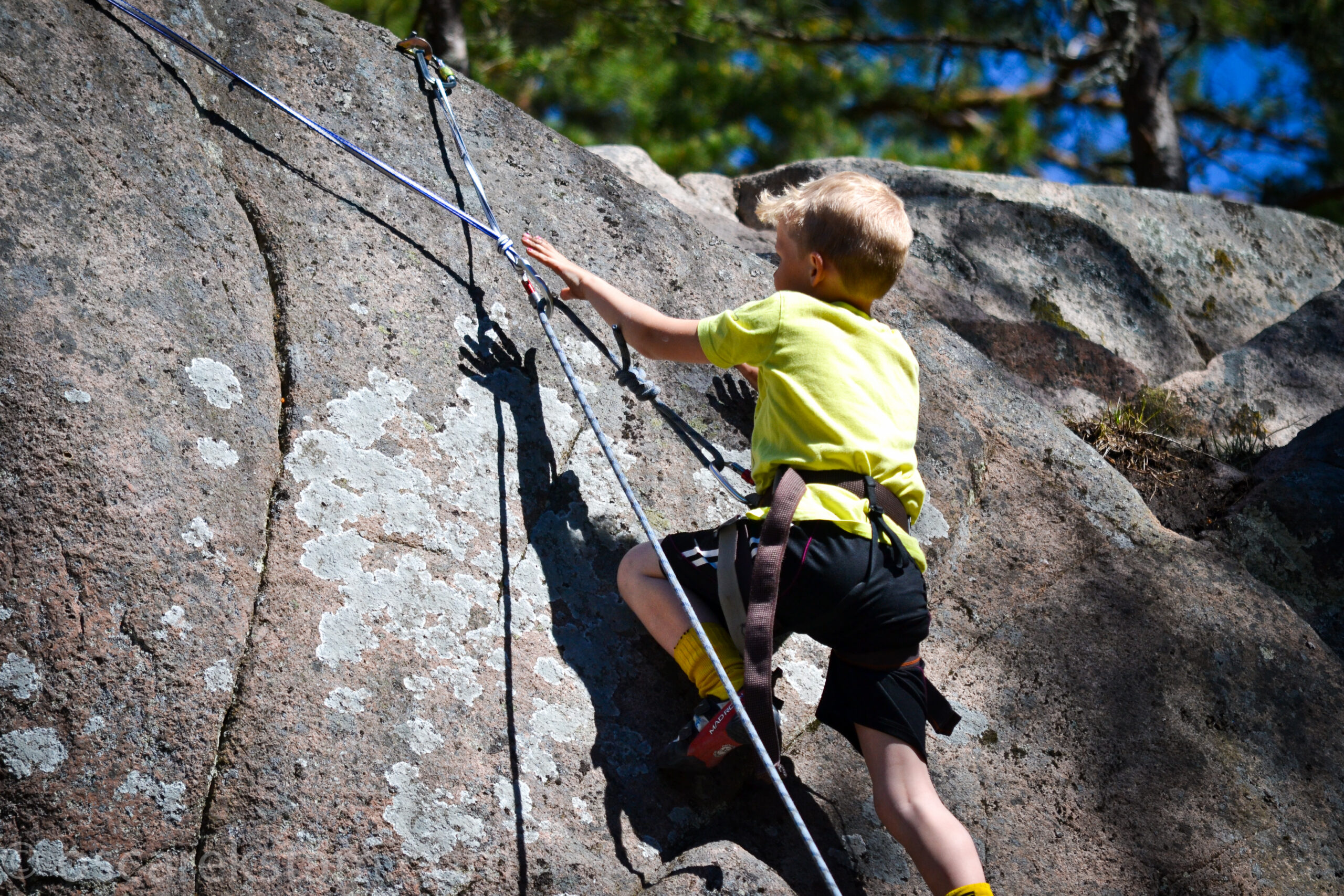 Ett barn klättrar med säkerhetslinor på bergsvägg i Långehäll.