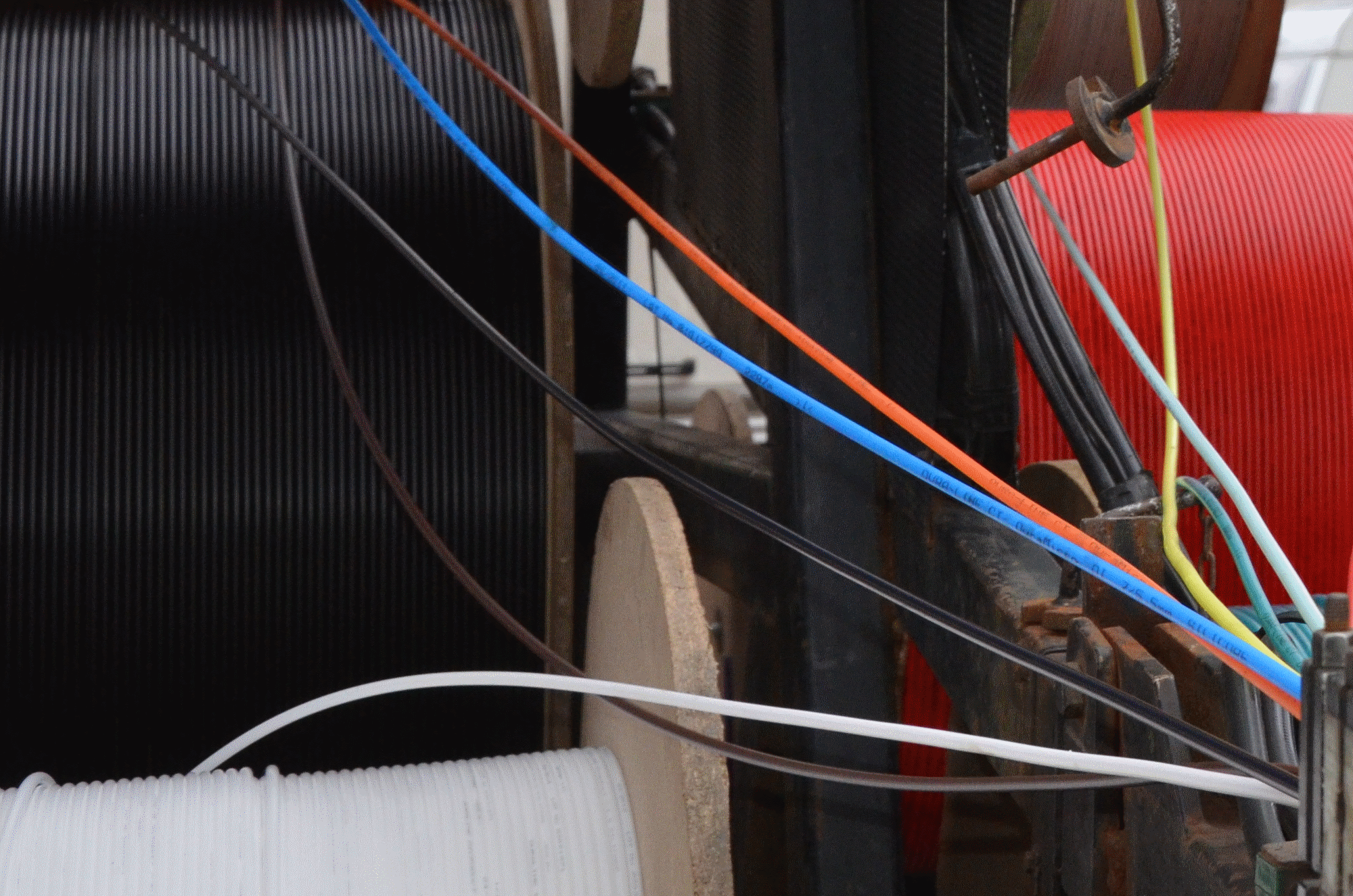 Färgade kablar för fiberanslutning. Kabeltrummorna står tätt i bakgrunden medan kablarna dras ut och läggs på plats vid fiberblåsningen.