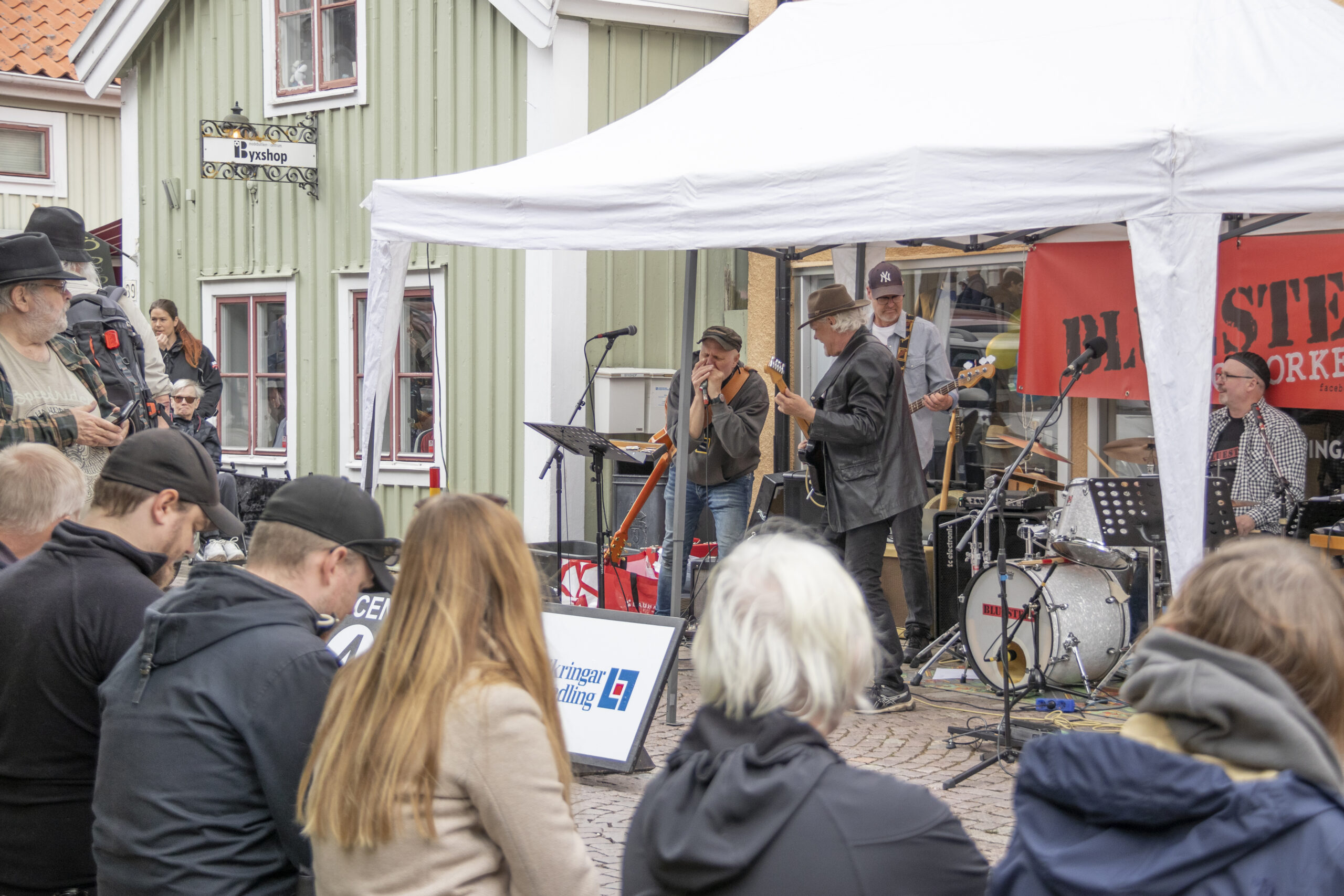 Ett band spelar i ett tält på en kullerstensgata. I förgrunden syns publiken.