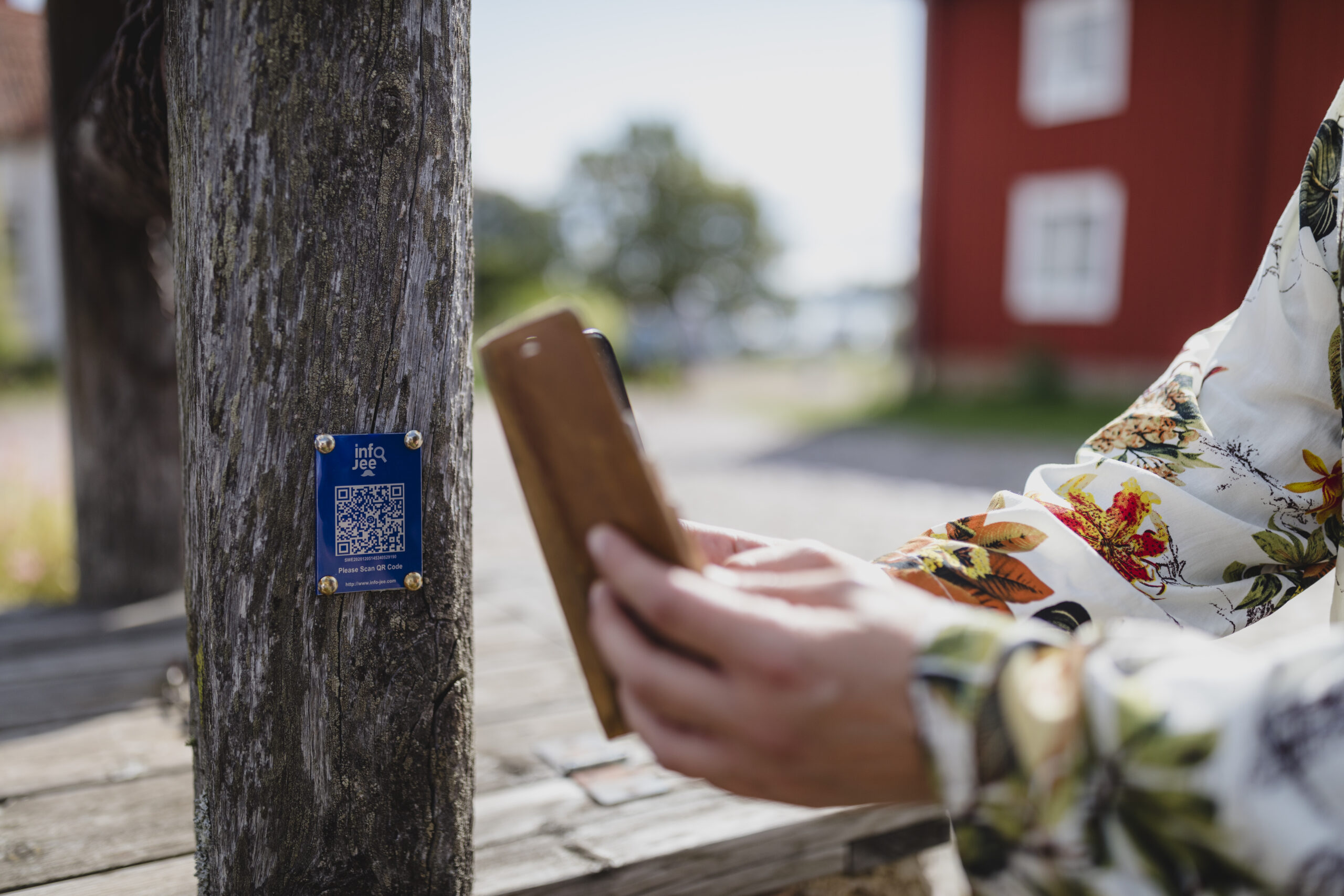 Två händer håller i en telefon framför en blå skylt med QR-kod