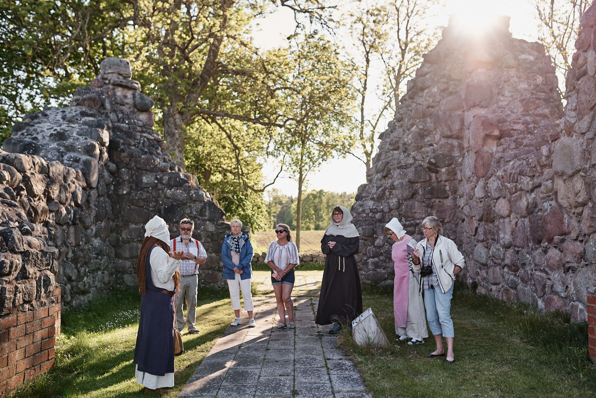 Medeltidsklädda guider tillsammans med besökare i en klosterruin av sten
