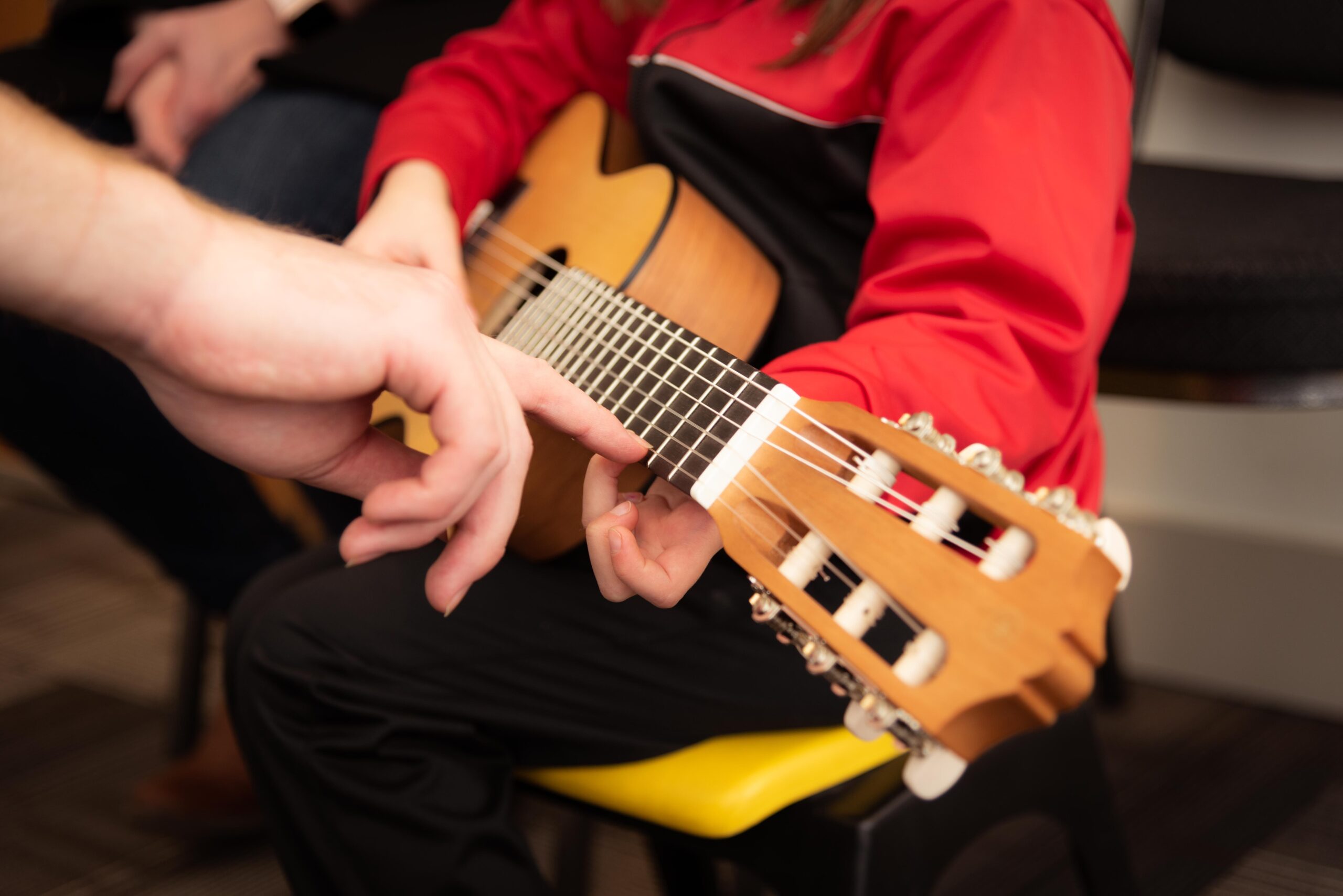 Barn spelar på gitarr. Blir hjälpt med ackord av en vuxen person.