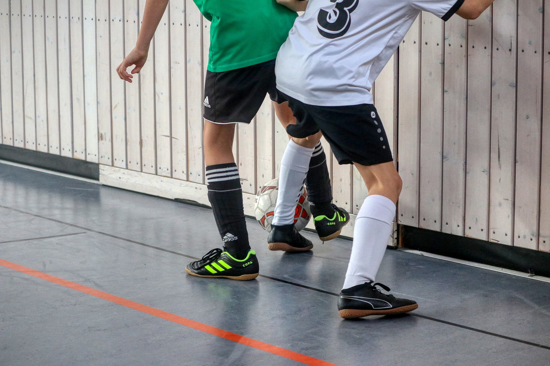 Barn spelar fotboll i en sporthall.