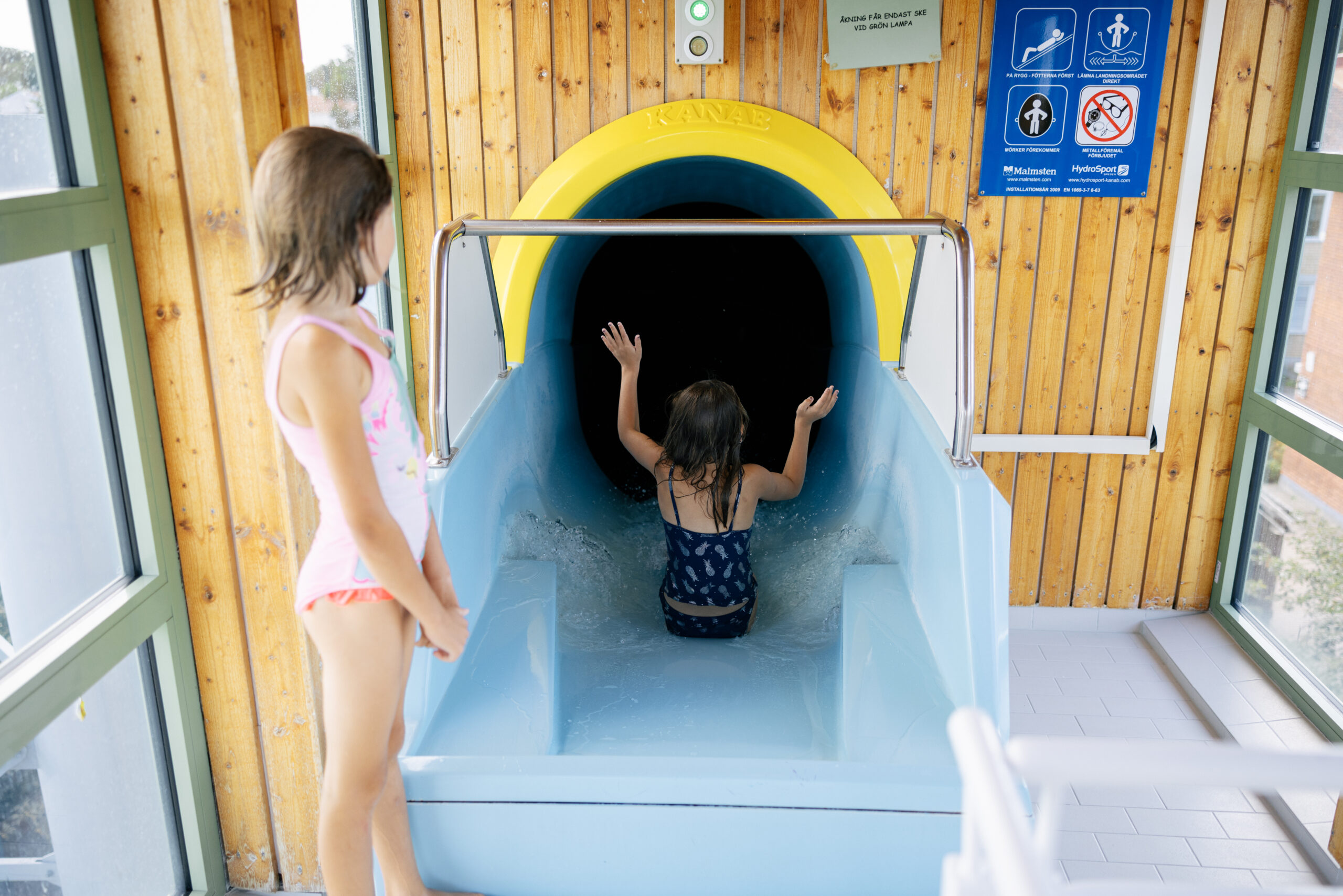 Två barn åker vattenrutschkana på simhallen.